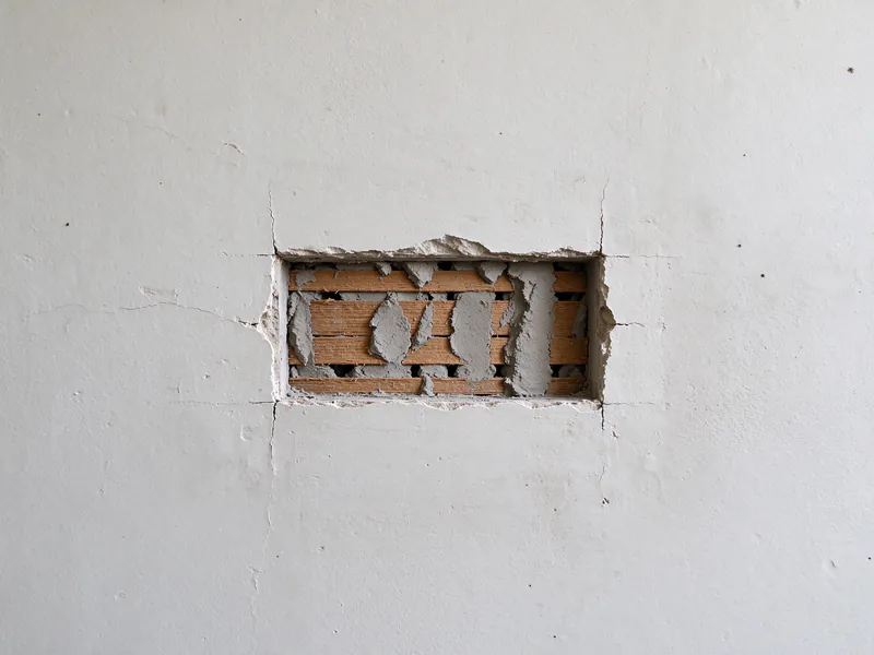 Close view inside a small plaster wall opening showing the wood lath strips and plaster keys