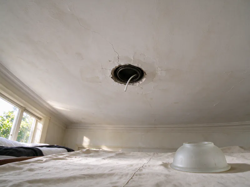 An open ceiling light box in a plaster ceiling with new white cable inside and the glass shade on a drop cloth below